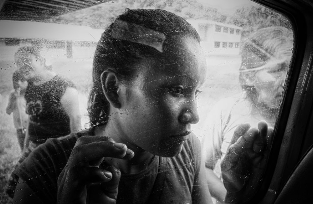 Date: 18 Jun 2017
Location: Morete Community, Pasataza Province, Ecuador.

A woman of the Sapara people looks through the window of a small plane that has just landed in the Morete community, on the Kichwa territory of the Ecuadorian Amazon. 

This territory is surrounded by thousands of acres of primary jungle, and is therefore only reachable through the air. There is no road, and it would take a person almost a week to get there by foot through muddy lands. The absence of a road is a blessing for the local people, as it enables them to control and preserve the territory, thus preventing its deforestation. 
The arrival of an airplane is a special happening, as it is the only contact with the "modern world".