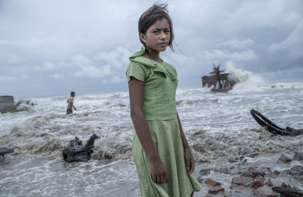 August 18, 2020: A girl, standing before her tea shop, which is completely ruined by sea water in Namkhana Island. After Cyclone Aila struck the Sundarbans in 2009, it became clear that frequent cyclonic events will turn the residents of Sundarbans into climate refugees. Within May 5, 2019 - May 25, 2021, Sundarbans faced cyclones- Fani, Bulbul, Amphan & Yaas – each devastating enough to justify the fear of mass displacement. In Indian Sundarbans, 54 of the 104 island support a human population of about 4.5 million. Extensive deforestation & a huge part of mangroves getting submerged has left little trees to shield the soil from high tides & heavy rains, increased soil erosion & reduced efficiency to prevent global warming & block cyclones resulting in huge destruction from Aila, Yaas & Amphaan. COVID-19-lockdown has left locals unemployed with no income. With time, ‘Sundarbans is destined to be the arena of the largest outward migration of humans in history.